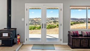 A room with a fireplace, a door leading to a patio, and a view of a hilly landscape.
