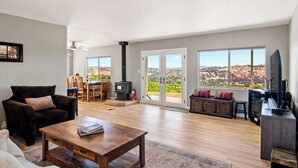 A spacious living room with a fireplace, large windows with a view of the countryside, a cozy seating area, and a television.