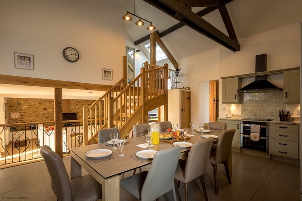 A dining area with a wooden staircase, a kitchen with modern appliances, and a stone wall in the background.