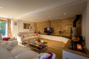 A cozy living room with a stone wall, a fireplace, a television, and a sofa.