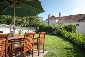 An outdoor patio with wooden furniture, a green umbrella, and a well-maintained lawn.