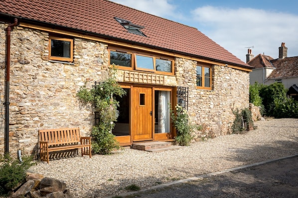 A stone house with a wooden door, a bench outside, and a gravel driveway.