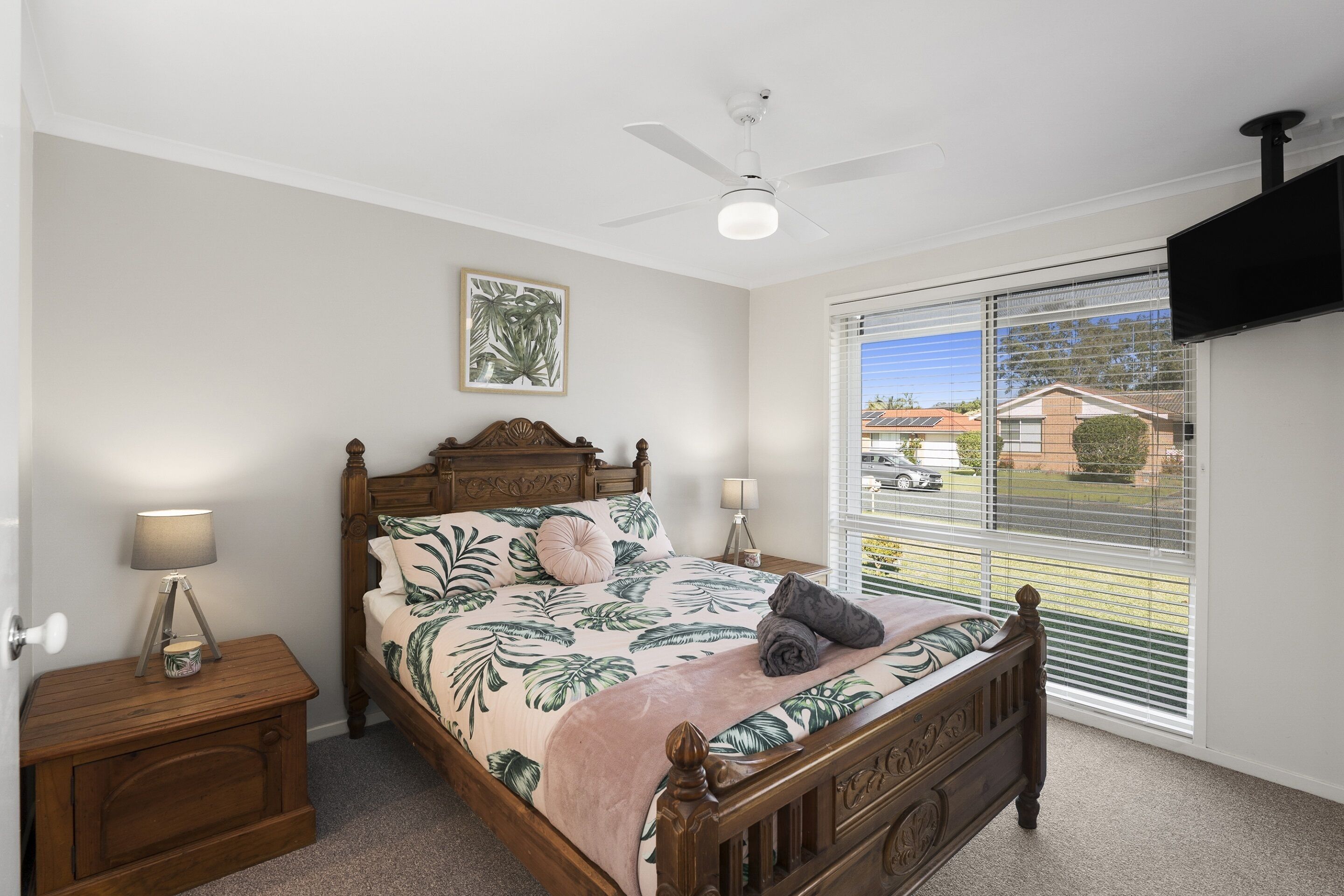 A bedroom with a bed, nightstand, lamp, ceiling fan, and a view through the window.