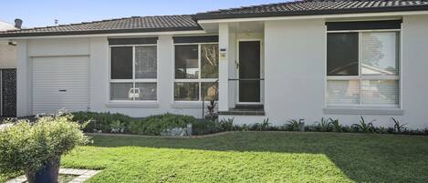 A single-story house with a white exterior, a garage door, and a well-maintained lawn.