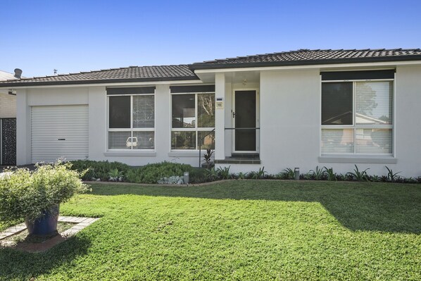 A single-story house with a white exterior, a garage door, and a well-maintained lawn. - Guest House on Guy (Forster)