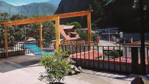 A wooden pergola, a swimming pool, and a potted plant on a terrace with a mountain backdrop.