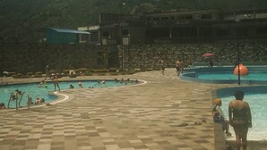 A pool area with multiple swimming pools, a checkered floor, and a mountainous backdrop.
