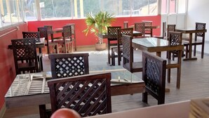 An indoor dining area with tables and chairs, a potted plant, and a view of the outside.