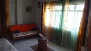 A room with a sofa, a small table, and a window with curtains. - Secret Haven TnT (Port of Spain)