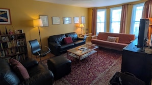 A living room with a black leather sofa, a red sofa, a coffee table, a bookshelf, and a television.