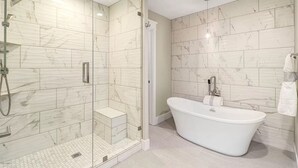 Une salle de bain moderne avec une baignoire sur pieds, une douche à parois de verre et des carreaux de marbre.