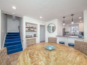 A modern kitchen with a round wooden table, a blue fish bowl, wicker chairs, and a staircase with blue steps.
