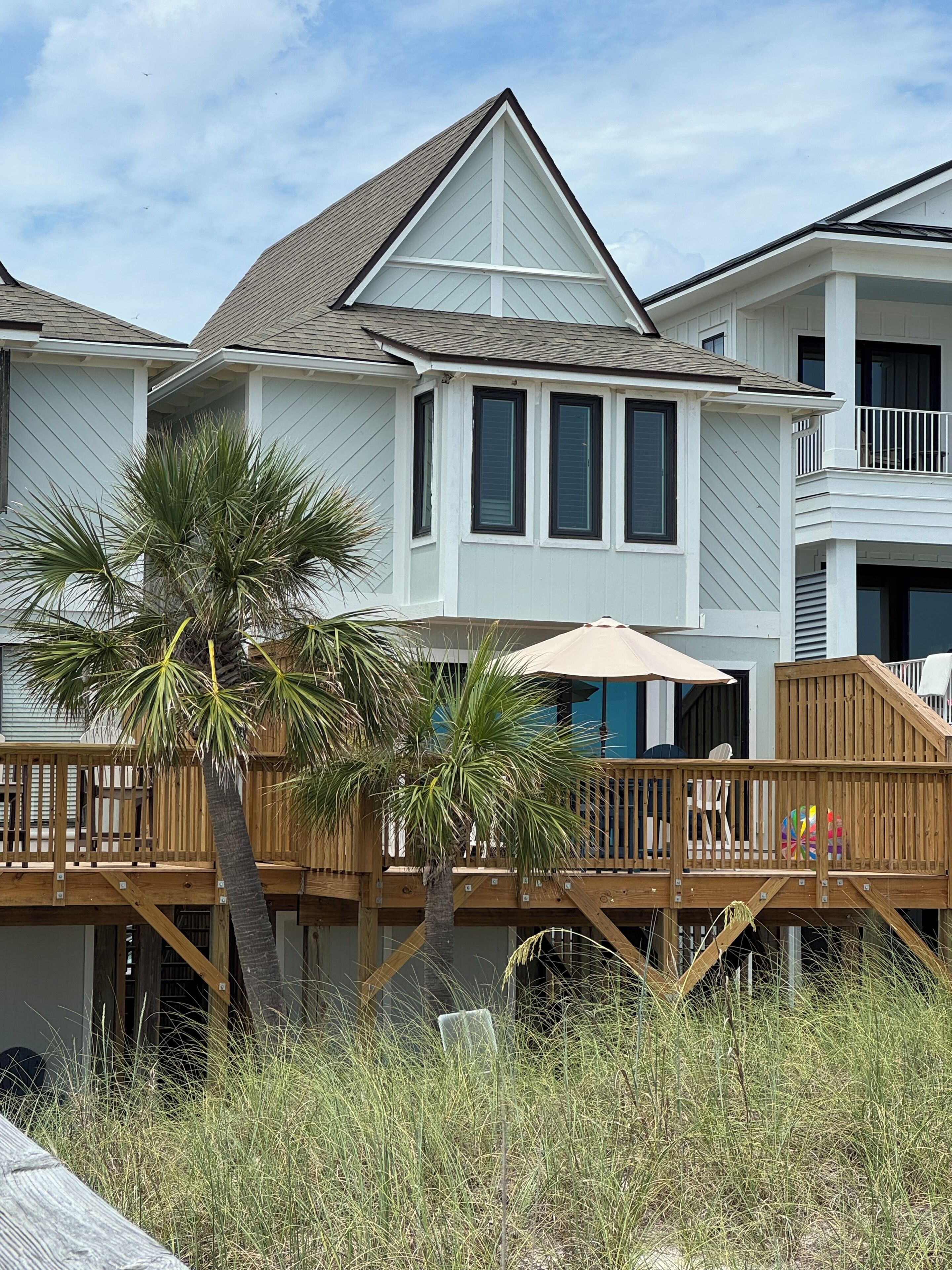 A two-story house with a balcony, a palm tree, and a wooden deck.