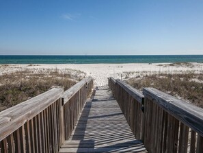 A wooden boardwalk leading to a beach with sand dunes and a clear blue sky.