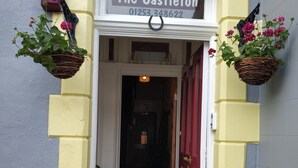A hotel entrance with a sign reading "The Castleton" and a phone number. There are potted plants on either side of the entrance. - The Castleton (Blackpool)