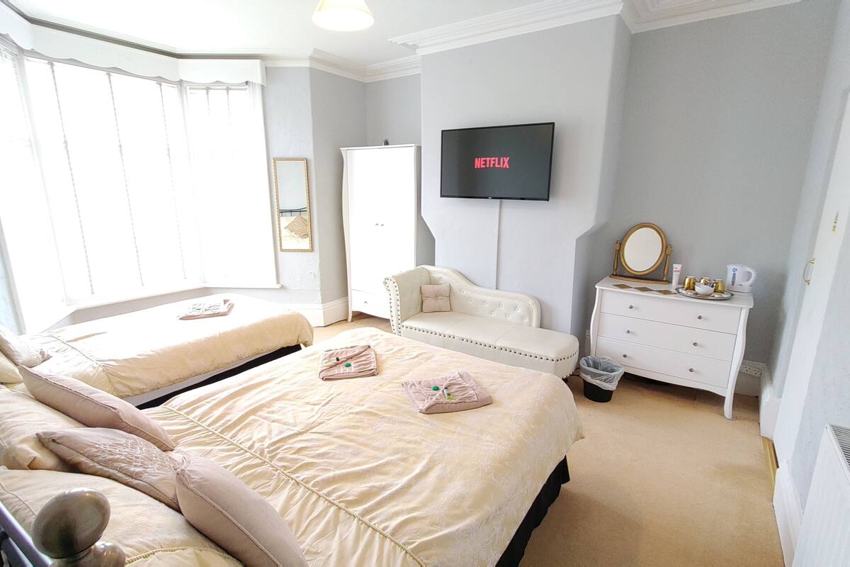 A hotel room with two beds, a TV, a dresser, and a window with curtains.