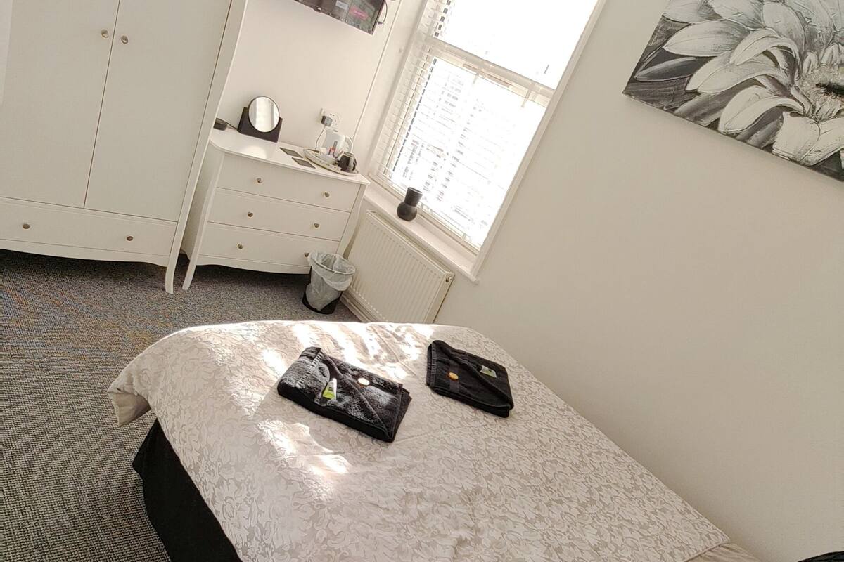 A bedroom with a bed, a dresser, a mirror, a window, and a painting.