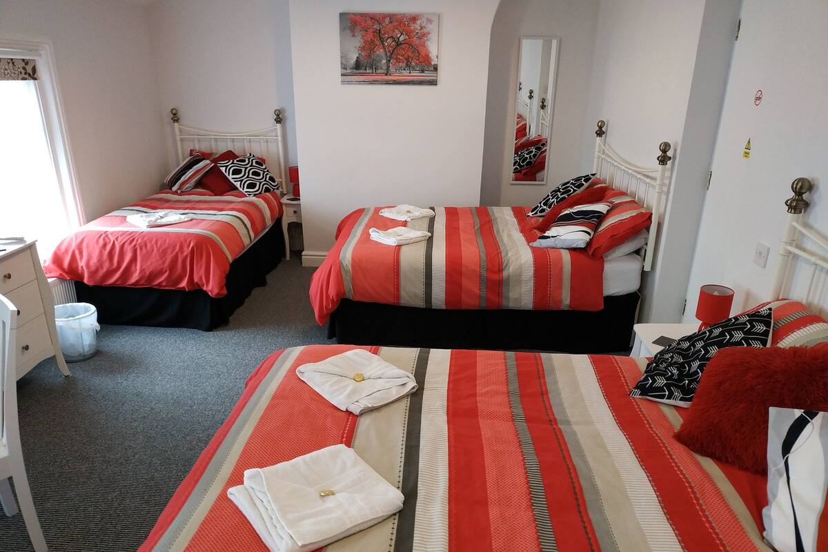 A hotel room with two beds, each with red and white striped bedding, a small desk, and a chair.
