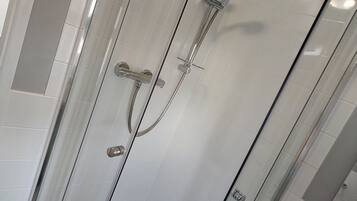 Una ducha con cerramiento de vidrio, cabezal de ducha de mano y grifo empotrado en la pared.