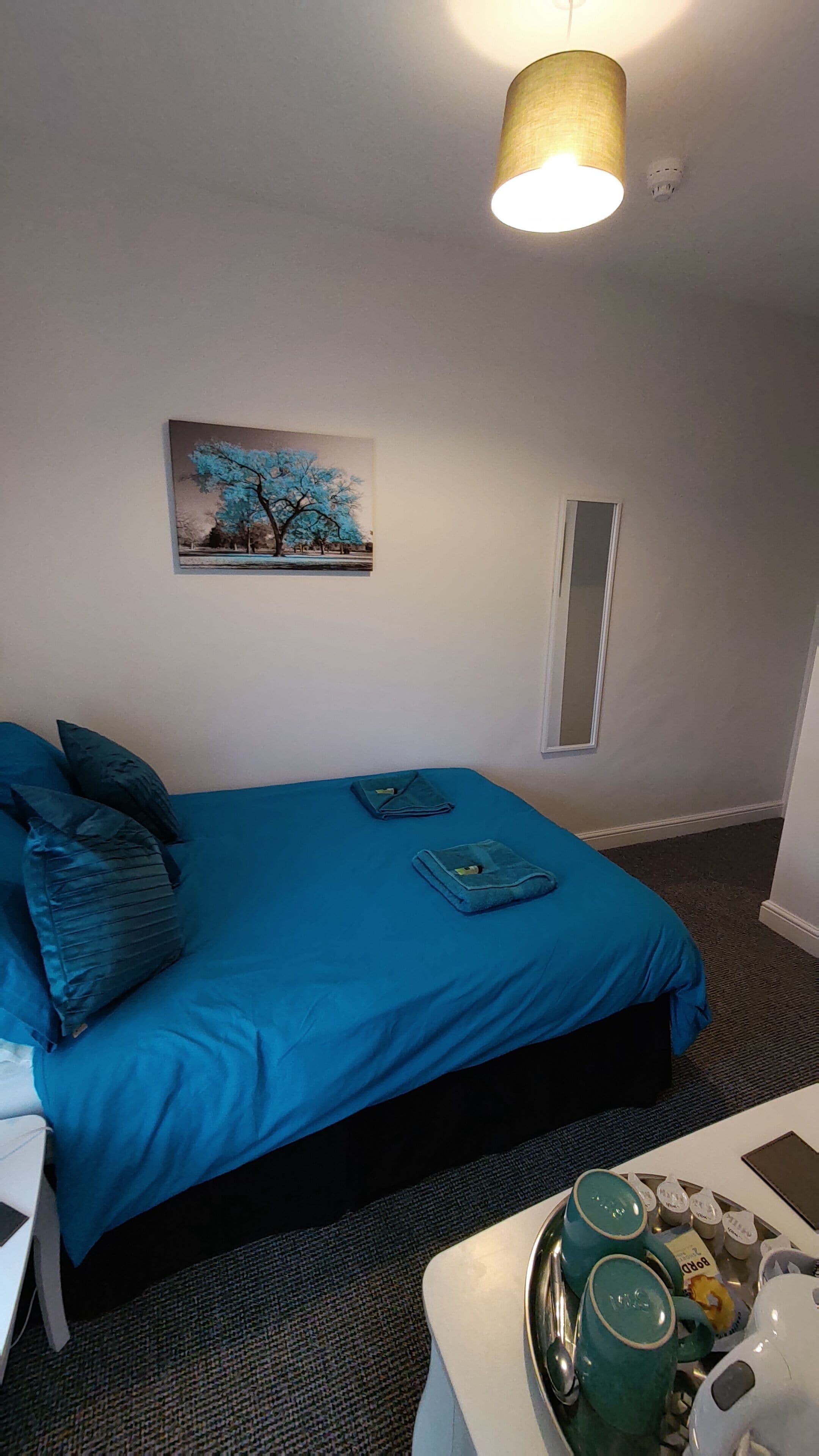 Una habitación con cama, un cuadro, una ventana y una mesa con una bandeja de objetos.