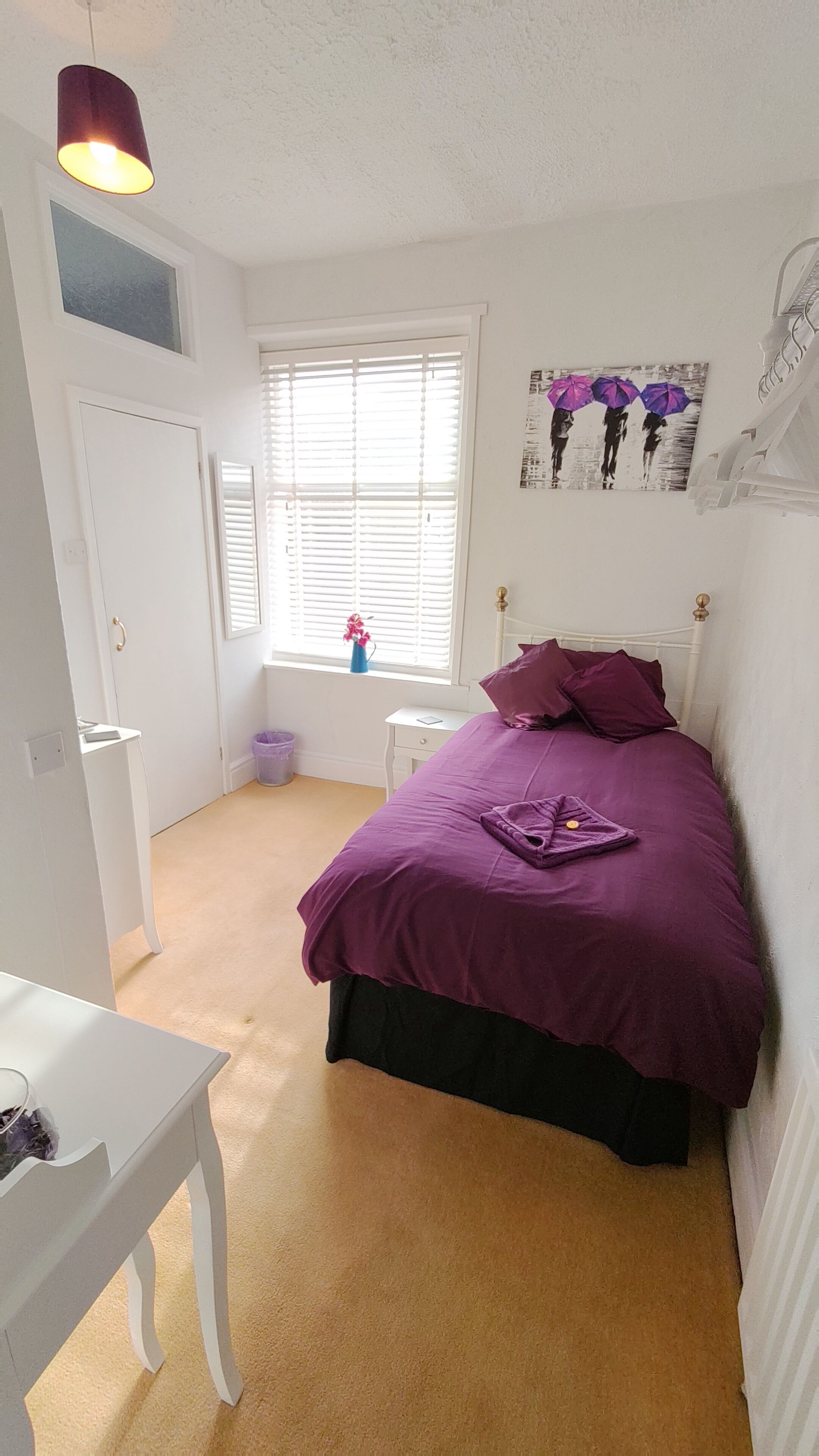 A bedroom with a bed, a nightstand, a window with blinds, a door, and a small table.