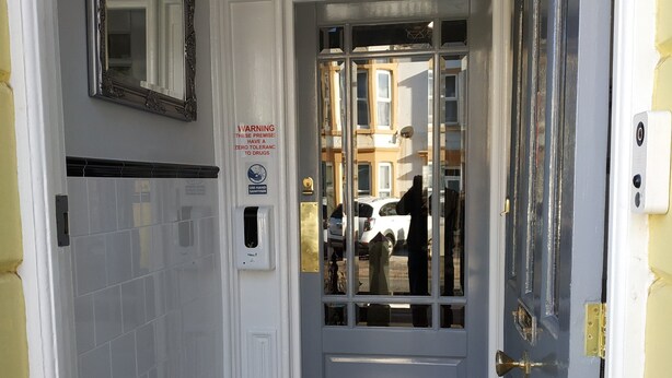 A hallway with a checkered floor, a door with a glass panel, and a warning sign about drug tolerance. - The Castleton (Blackpool)
