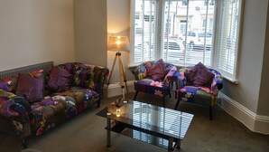 A cozy living room with a patterned sofa, a glass coffee table, and a floor lamp. - The Castleton (Blackpool)