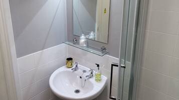 Un baño con lavamanos blanco, espejo y cabina de ducha de vidrio.
