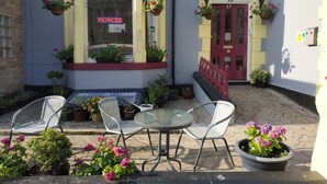 A corner building with a 'VACANCIES' sign, outdoor seating with chairs and a table, and hanging flower baskets. - The Castleton (Blackpool)