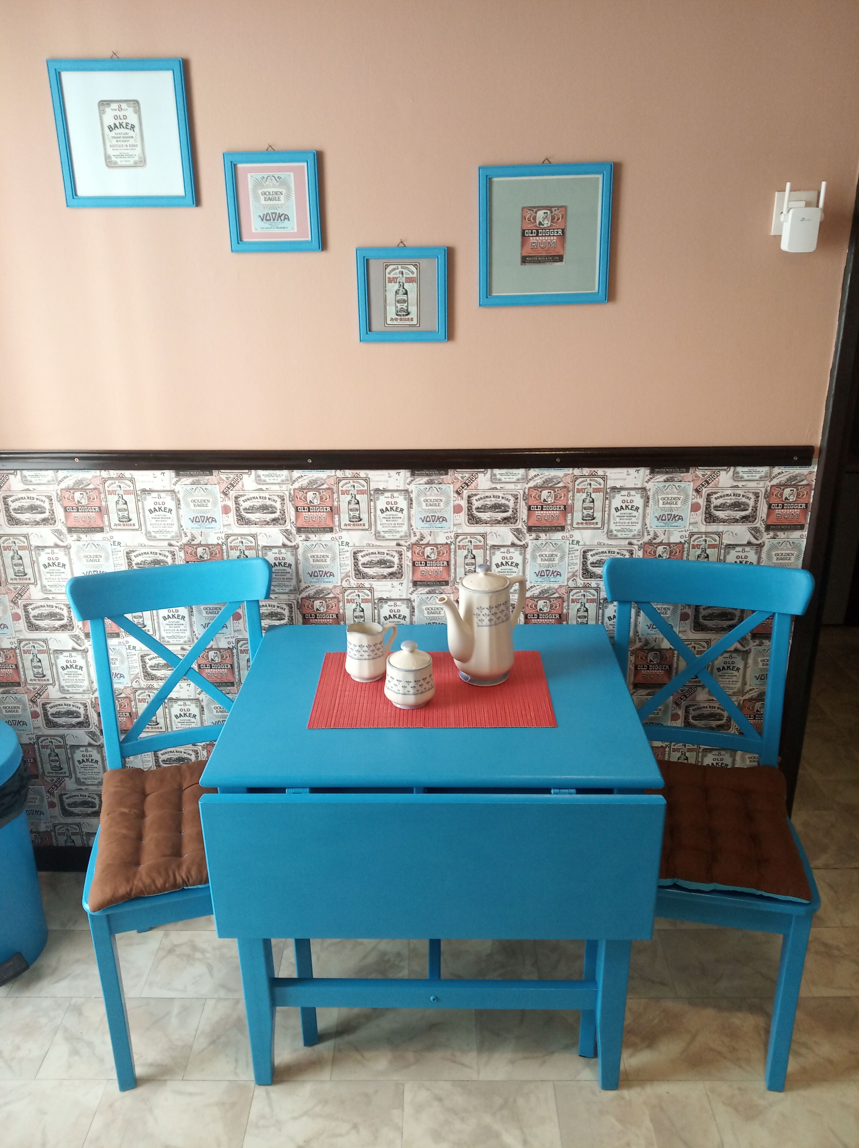 Ein blauer Tisch mit einer roten Tischdecke, zwei blaue Stühle und eine Wand mit Vintage-Tapete.