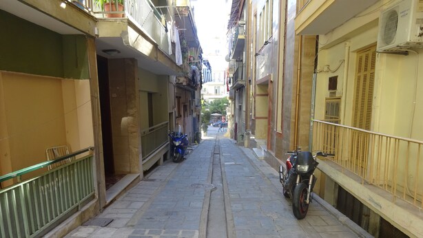 A narrow street with buildings on either side, a motorcycle parked on the right, and a metal fence on the left. - Cosy Penthouse (up to 6 guests) in the City Centre! (Thessaloniki)