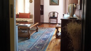A cozy living room with a wooden floor, a patterned rug, a sofa, a chair, a bookshelf, and a painting on the wall. - Cosy Penthouse (up to 6 guests) in the City Centre! (Thessaloniki)