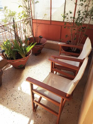 Un espacio al aire libre con mesas y sillas de madera, y plantas en macetas, bañado por el sol.