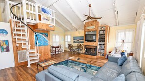 A spacious living room with a blue sofa, wooden staircase, and a bookshelf. - Oceanside, Pool, Close to Beach, Sun Decks, OS1E, Seas The Day (Corolla)