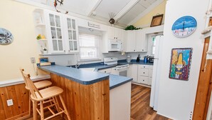 A kitchen with white cabinets, a blue countertop, wooden stools, and a refrigerator with a decorative magnet. - Oceanside, Pool, Close to Beach, Sun Decks, OS1E, Seas The Day (Corolla)