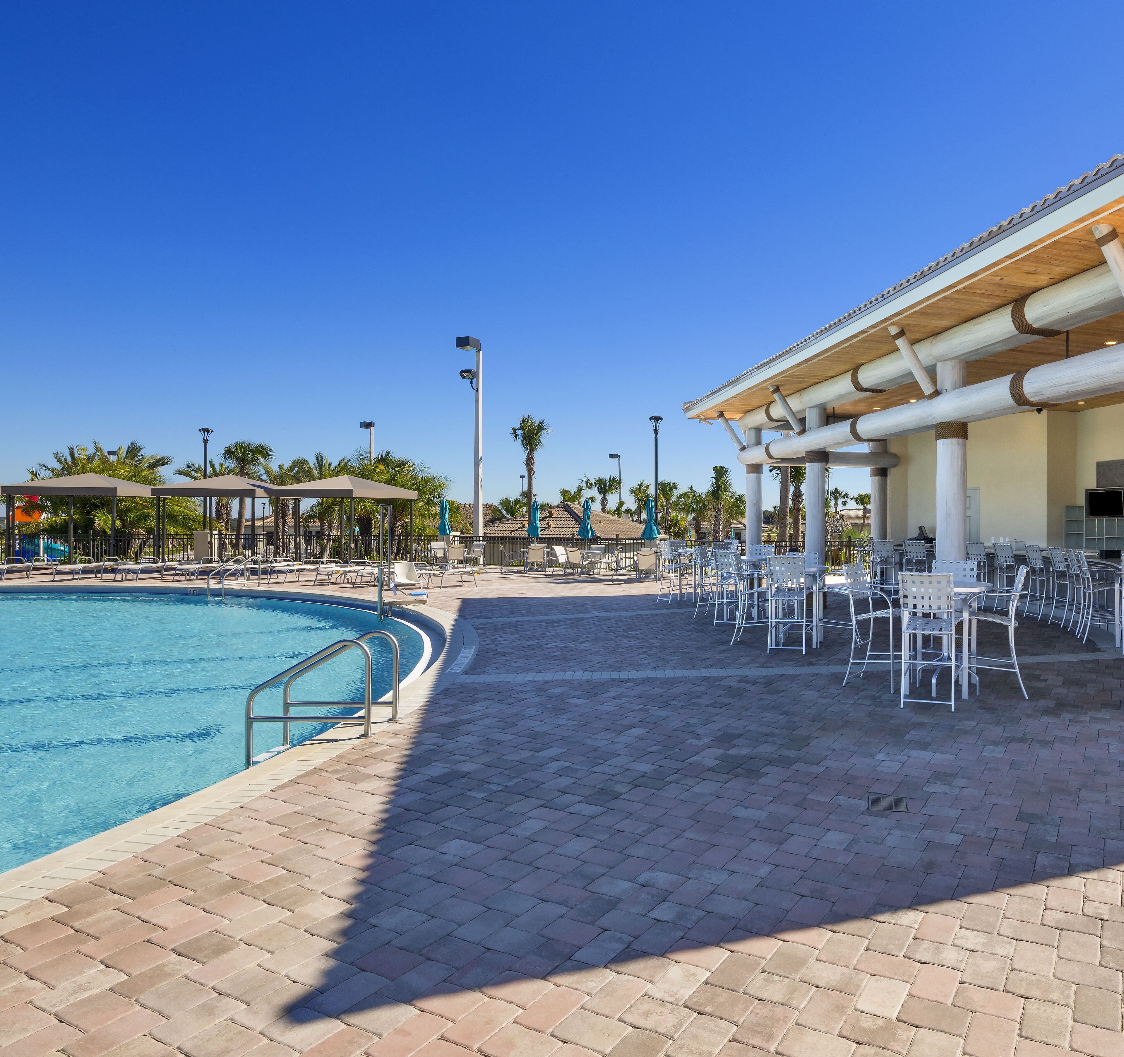 A pool area with a tiled deck, lounge chairs, and umbrellas.