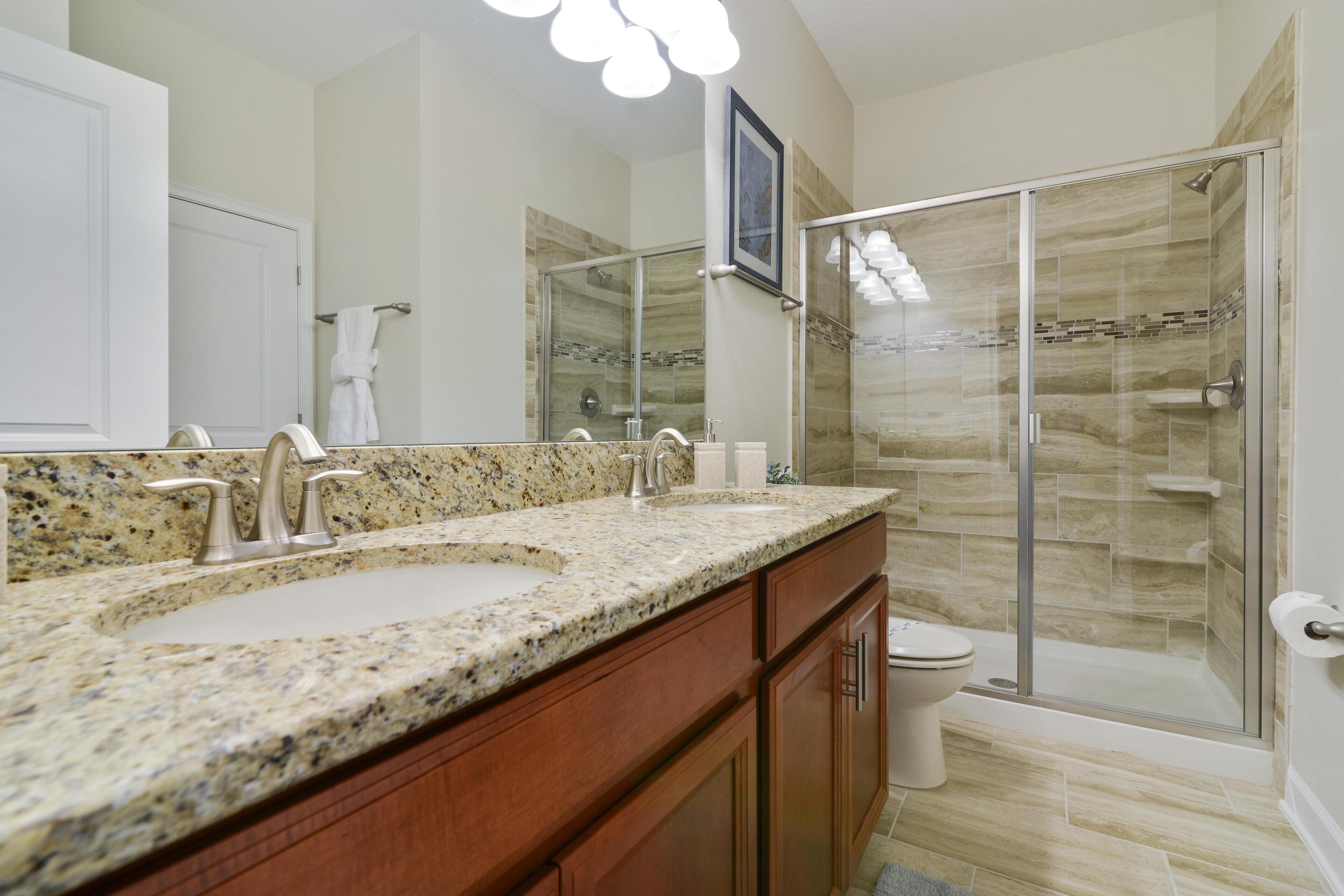 A bathroom with a granite countertop sink, a glass shower enclosure, and wooden cabinets.