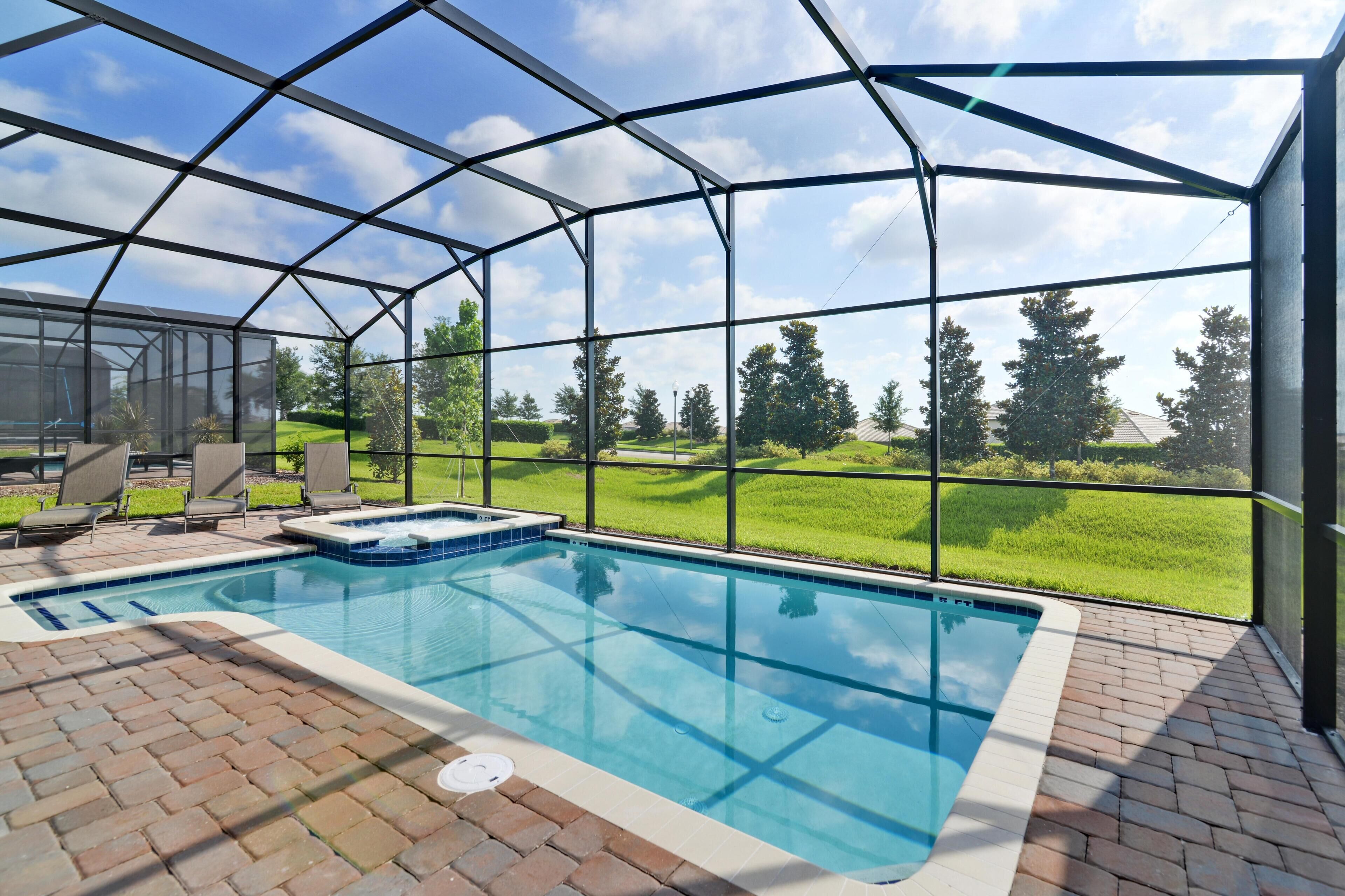 Piscina com cobertura de vidro, rodeada por um pátio de tijolos e móveis de exterior.