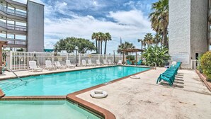 A swimming pool with lounge chairs, a fenced area, and palm trees. - Seaside Corpus Christi Condo at The Villa del Sol! (Corpus Christi)
