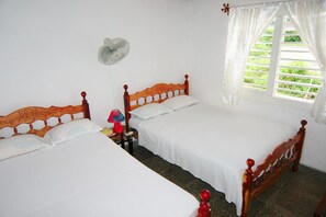 Two single beds with floral headboards and white linens, a bedside table and lamp, and a wall-mounted fan.