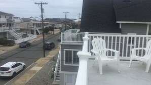A residential area with a house featuring a balcony with white chairs, a driveway with cars, and a street with houses in the background. - Walk to the ocean and Boardwalk (Seaside Park)