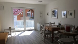 A spacious room with a wooden dining table, chairs, a sofa, and a large sliding glass door leading to an outdoor area. - Apartment Schönblick (Pfronten-Halden)