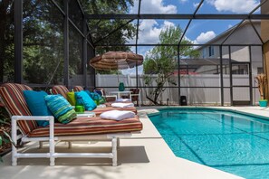 Un área junto a la piscina con sillones de descanso y una sombrilla.