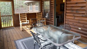 Eine Holzhütte mit Glastisch und Stühlen, einer Holzterrasse und großen Fenstern.