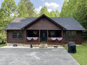 Cozy cabin with a central entrance, flanked by two windows, and a patriotic flag on the front porch.