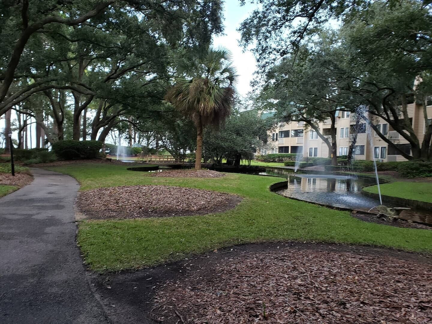 A park with a paved walkway, a pond, and a fountain.