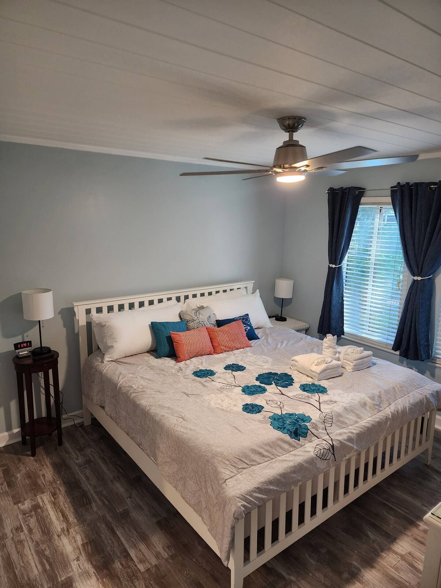 A bedroom with a white bed, blue curtains, and a ceiling fan.