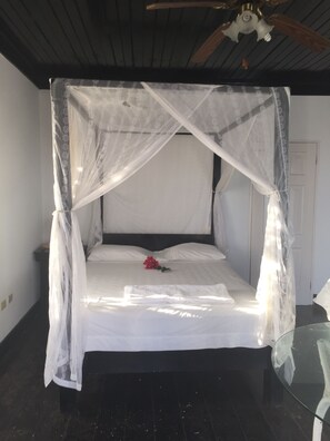 Ein Bett mit Baldachin, ein Glastisch und ein Deckenventilator.