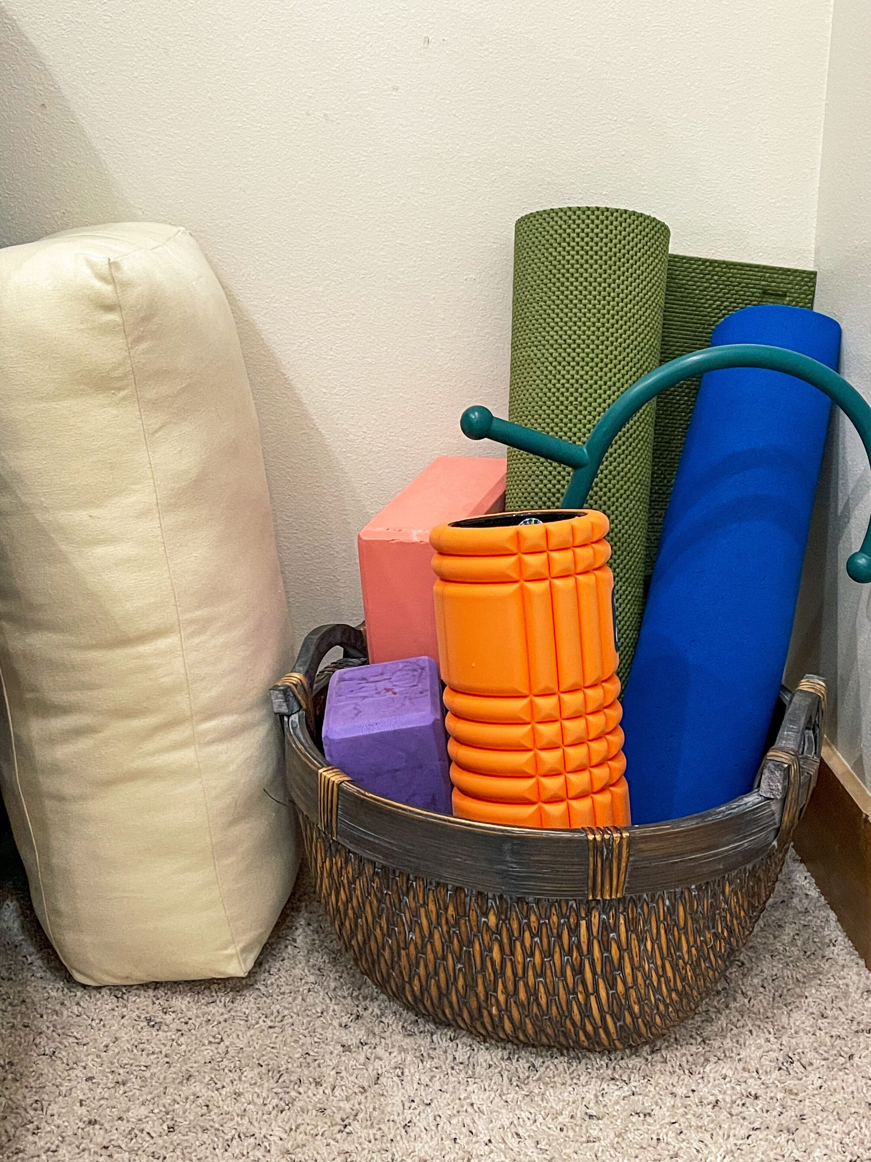 Un panier en osier contenant différents tapis de sol pour la pratique d’exercices et un coussin blanc.