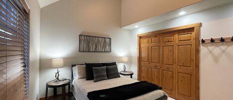 A bedroom with a large bed, two bedside tables, a wooden wardrobe, and a wall-mounted artwork.